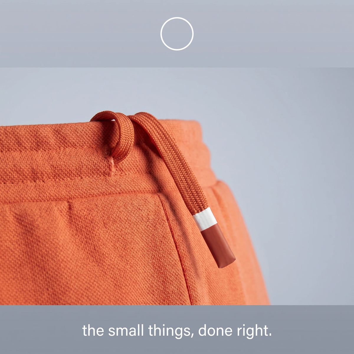 Close-up of an orange textured fabric garment with a matching drawstring and a white-and-orange tip, shown against a light gray background with text at the bottom reading 'the small things, done right.'.