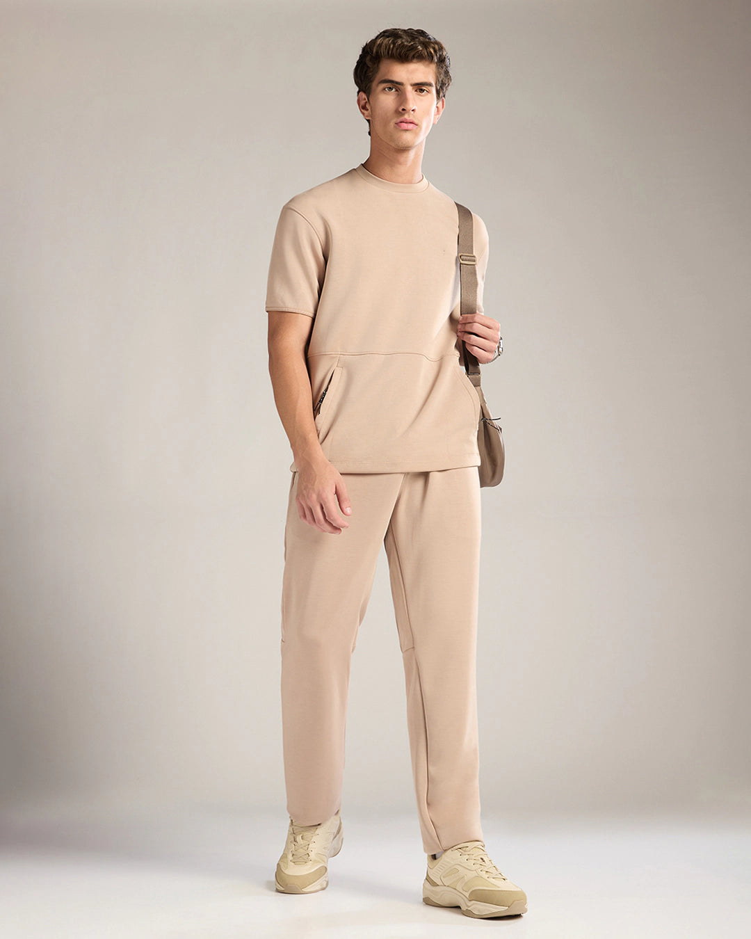 Man wearing a beige outfit with a bag against a neutral background