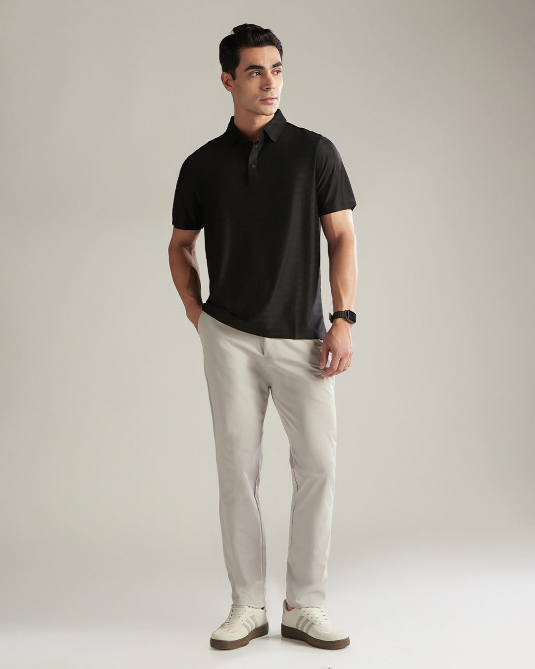 Man wearing a black polo shirt and light gray pants against a plain background