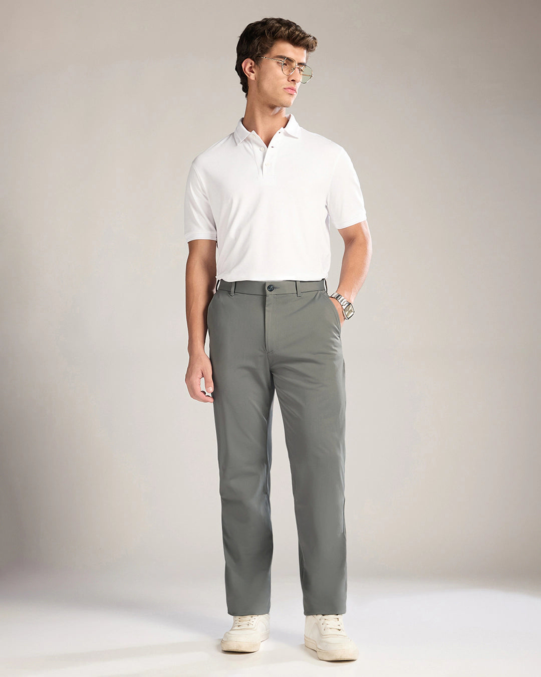 Man wearing a white polo shirt and gray pants against a plain background