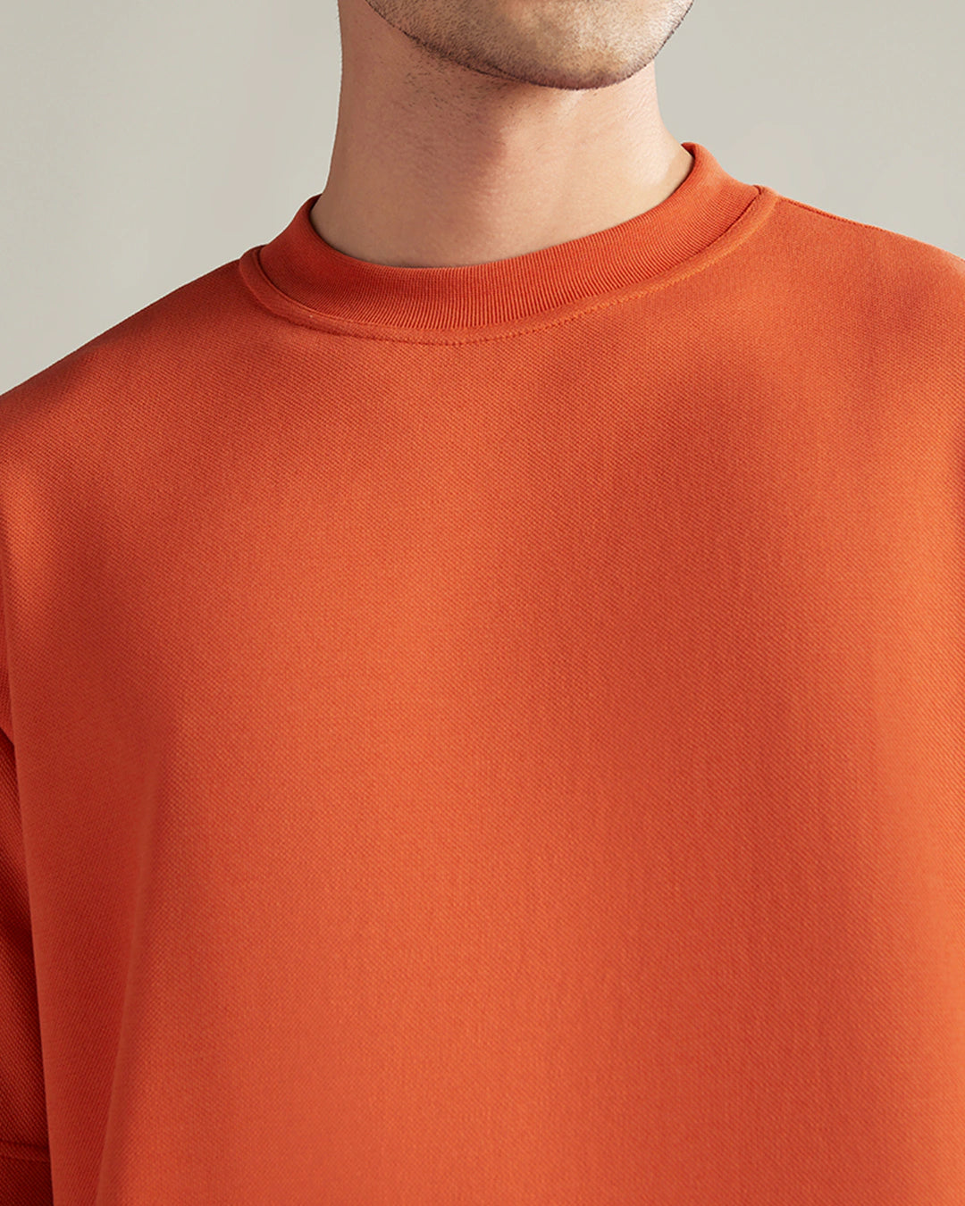 Close-up of a person wearing an orange sweater against a neutral background