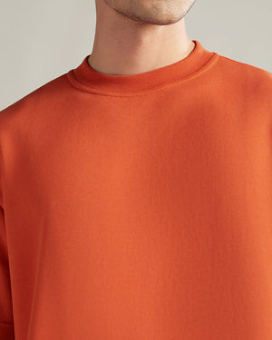 Close-up of a person wearing an orange sweater against a neutral background