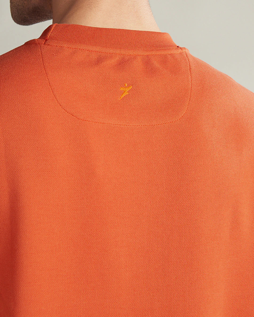 Close-up of an orange polo shirt with a small logo on the collar against a neutral background