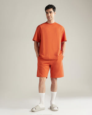 Man wearing an orange outfit with shorts and a t-shirt on a plain background