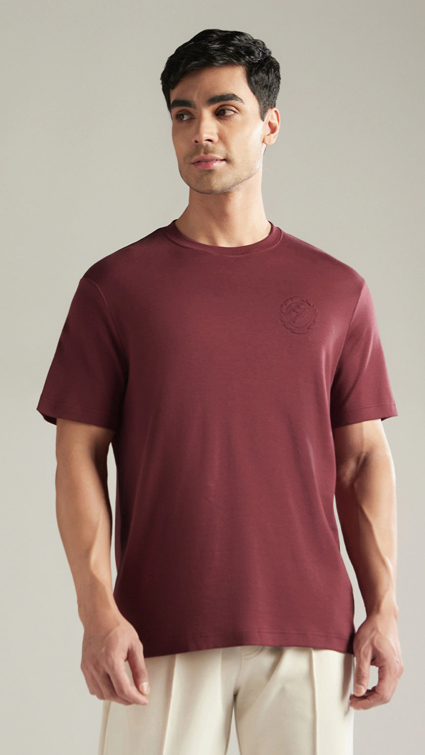 Man wearing a maroon t-shirt with a logo on a plain background