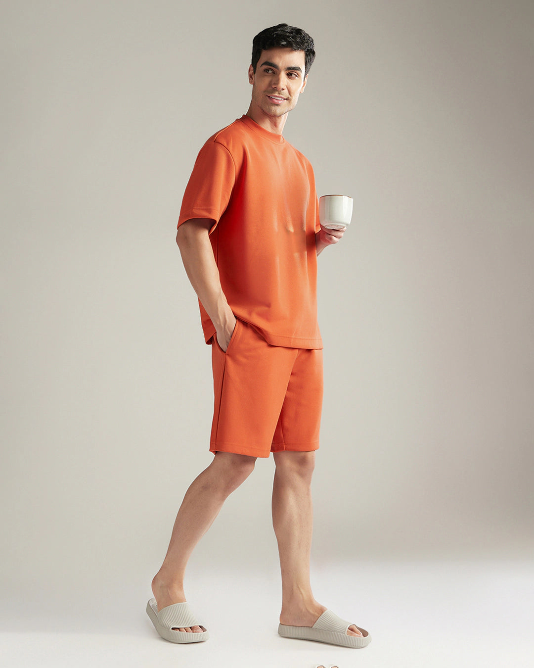 Man wearing an orange outfit holding a white cup against a plain background