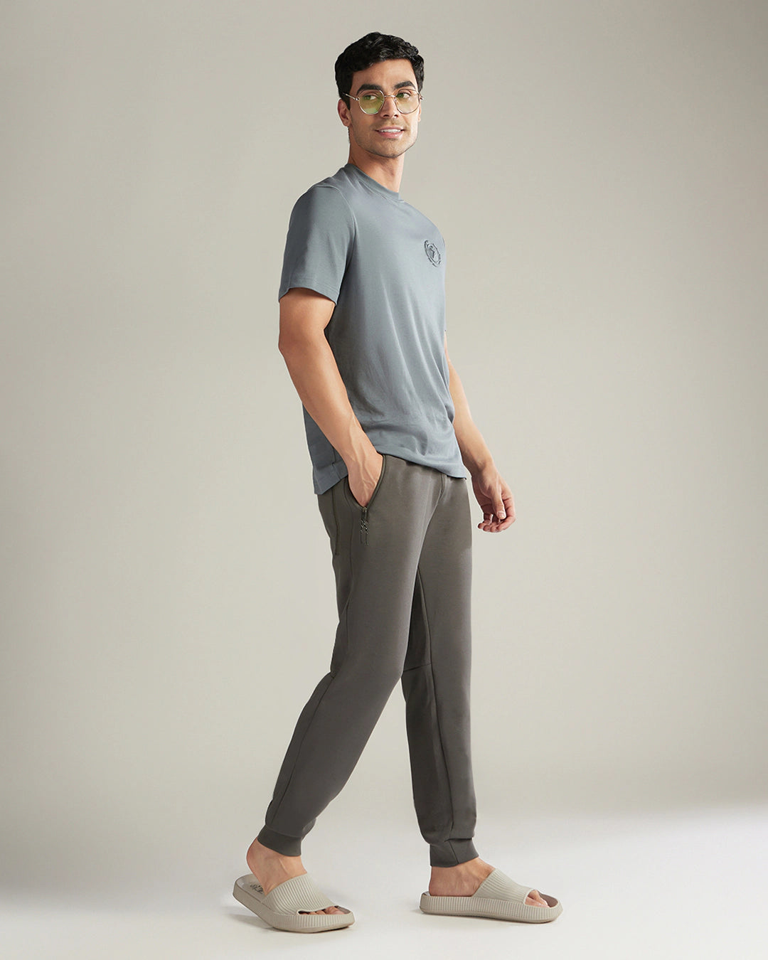 Man wearing a gray t-shirt and dark gray jogger pants against a plain background