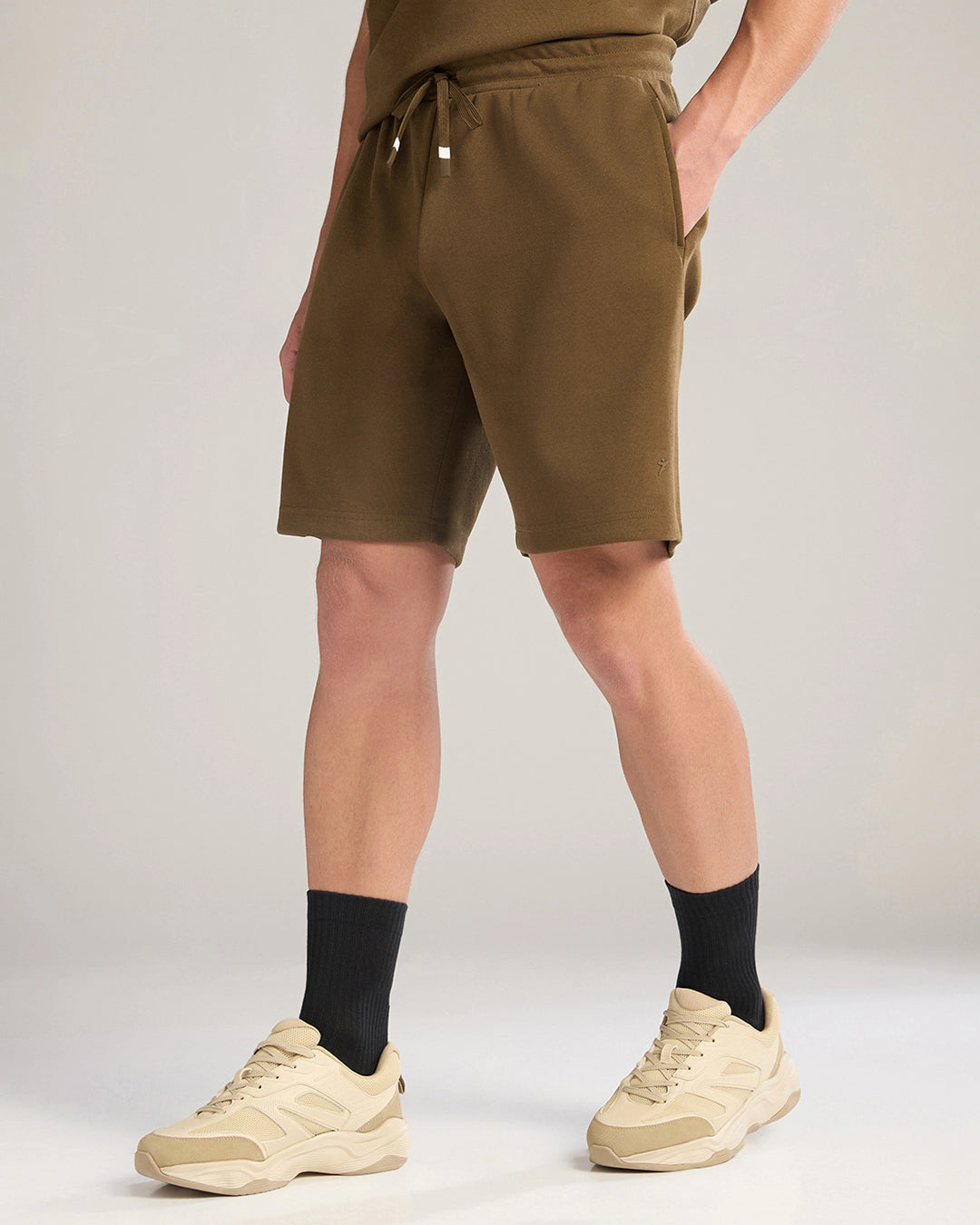 Person wearing brown shorts, black socks, and beige sneakers on a plain background