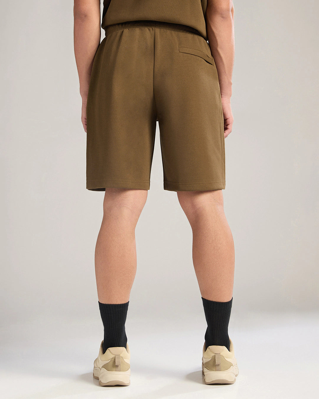 Person wearing brown shorts on a plain background