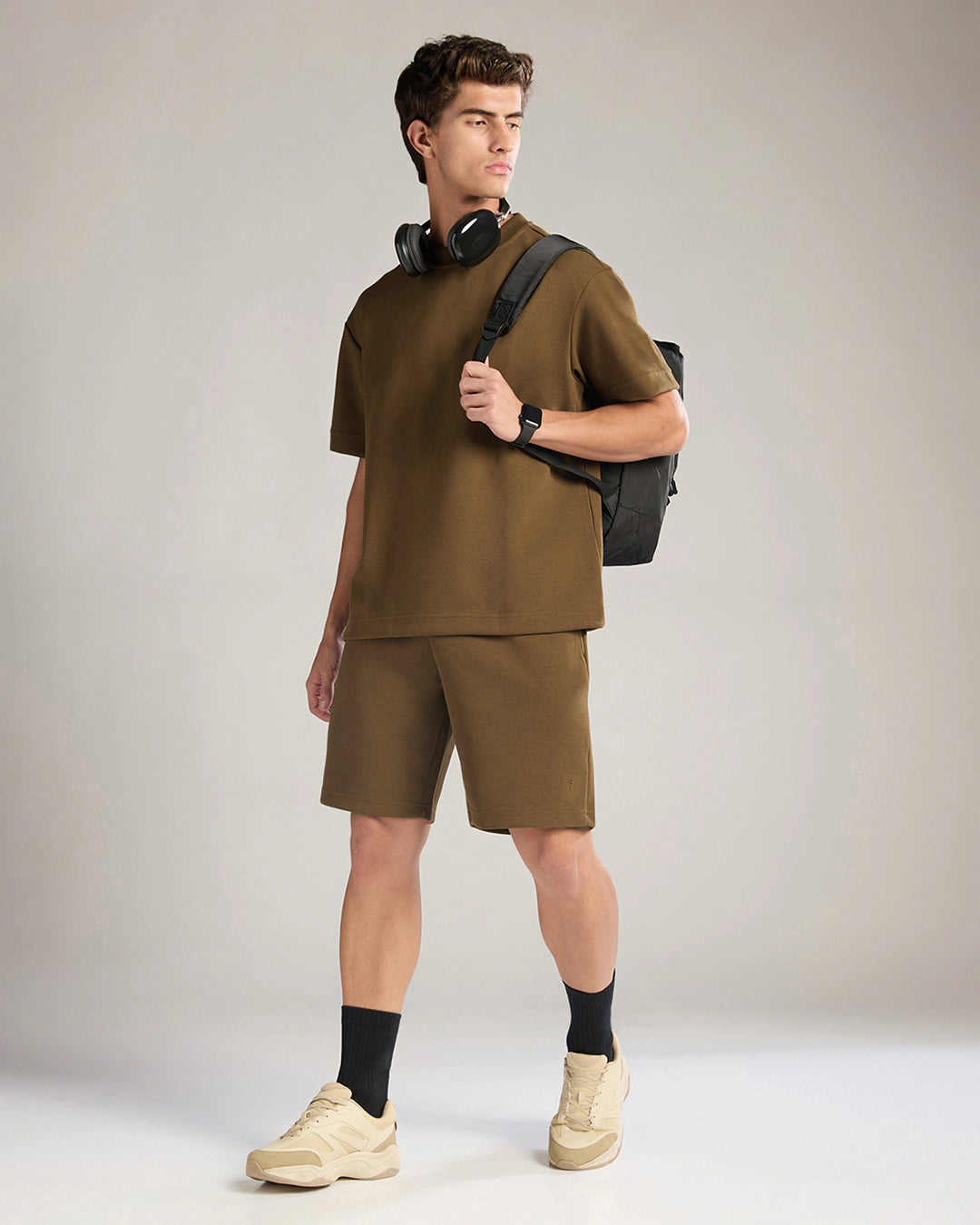 Man wearing a brown outfit with a black backpack on a plain background