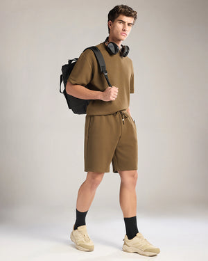 Man wearing a green outfit with a backpack and headphones on a plain background