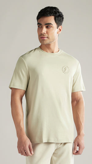 Man wearing a light green t-shirt with a logo on a plain background