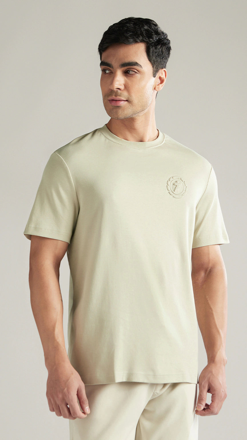 Man wearing a light green t-shirt with a logo on a plain background