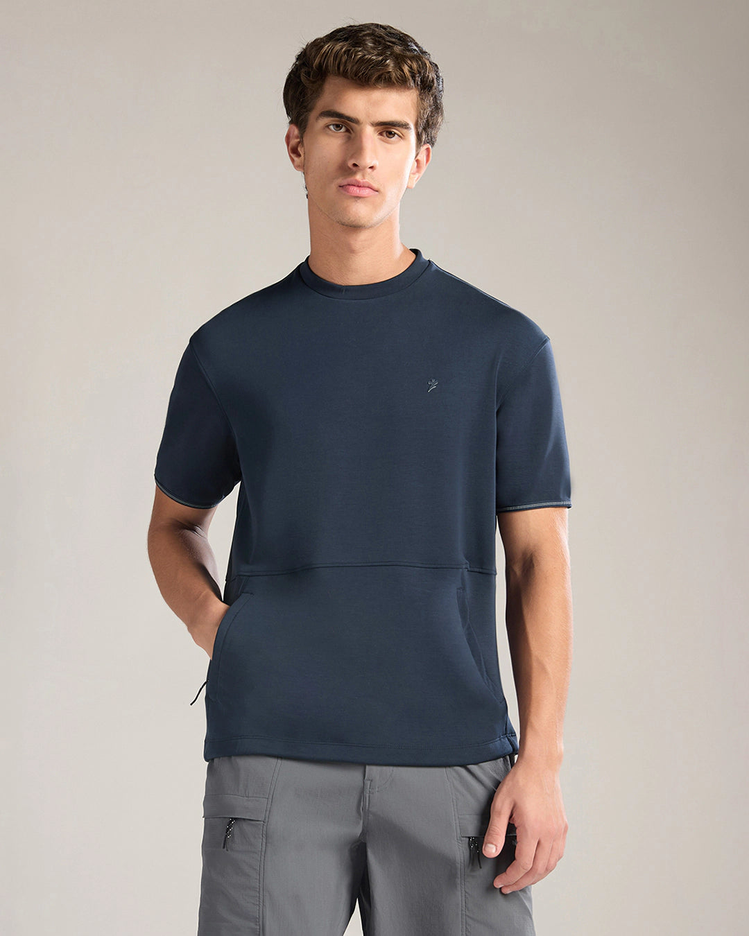 Man wearing a navy blue t-shirt and gray pants against a plain background