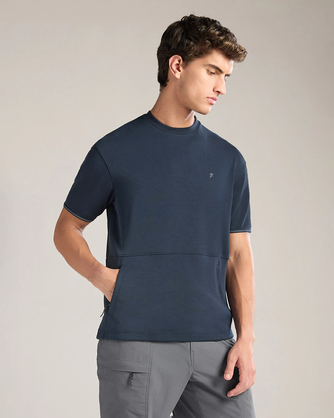 Man wearing a navy blue short-sleeve shirt and gray pants on a beige background