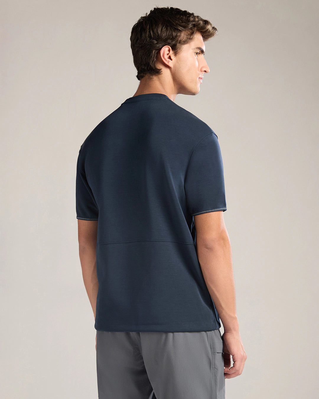 Man wearing a navy blue t-shirt and gray pants against a plain background