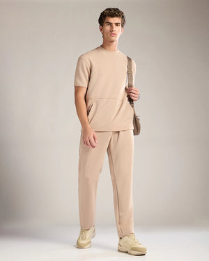 Man wearing a beige outfit with a bag against a neutral background