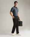 Man wearing a gray polo shirt and black pants, holding a black briefcase against a neutral background