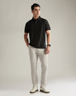 Man wearing a black polo shirt and light gray pants against a plain background