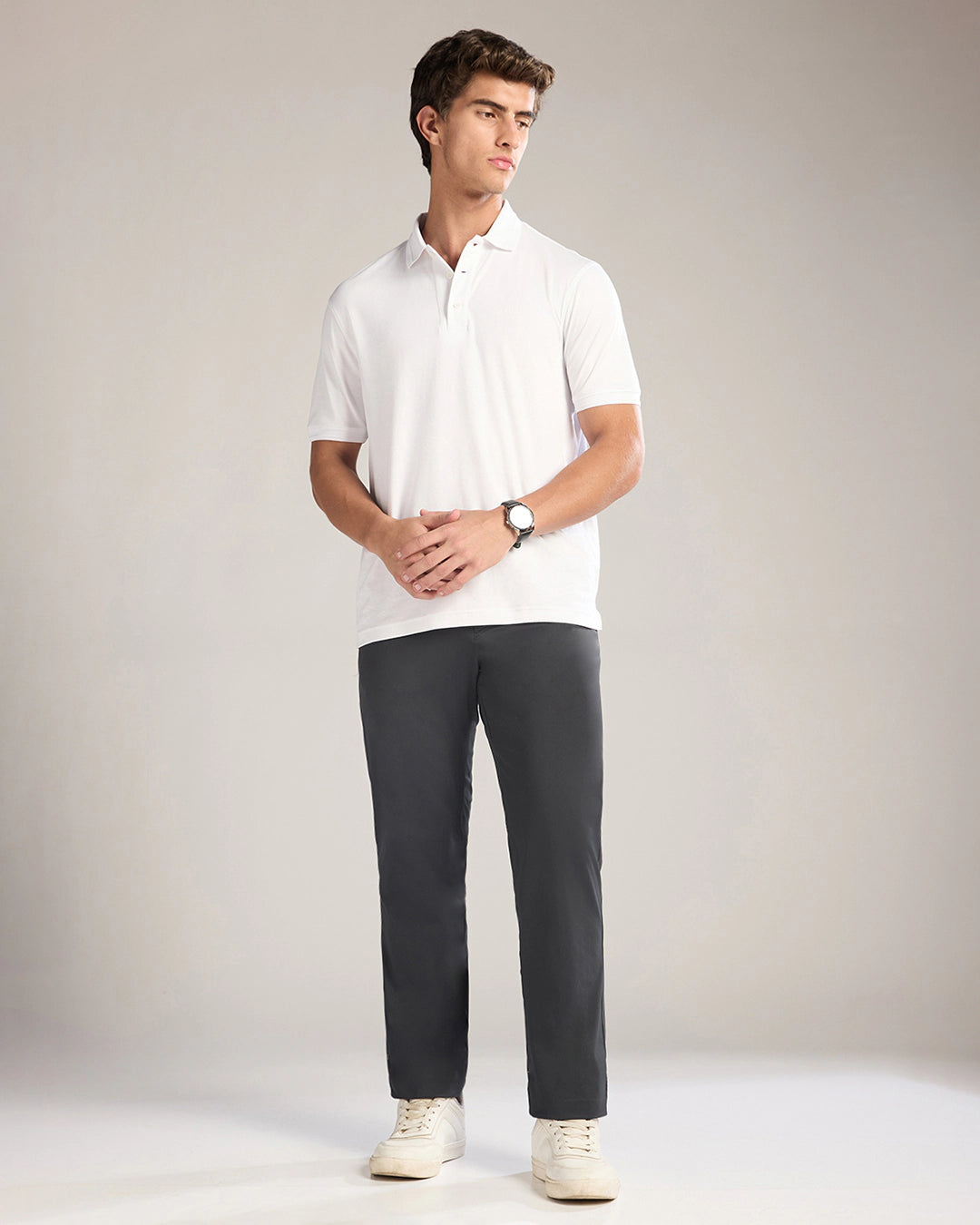 Man wearing a white polo shirt and dark gray pants on a plain background