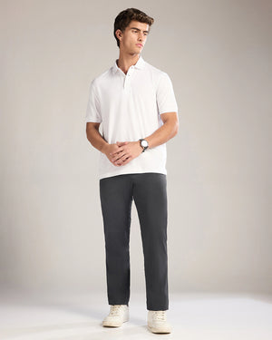 Man wearing a white polo shirt and dark gray pants on a plain background