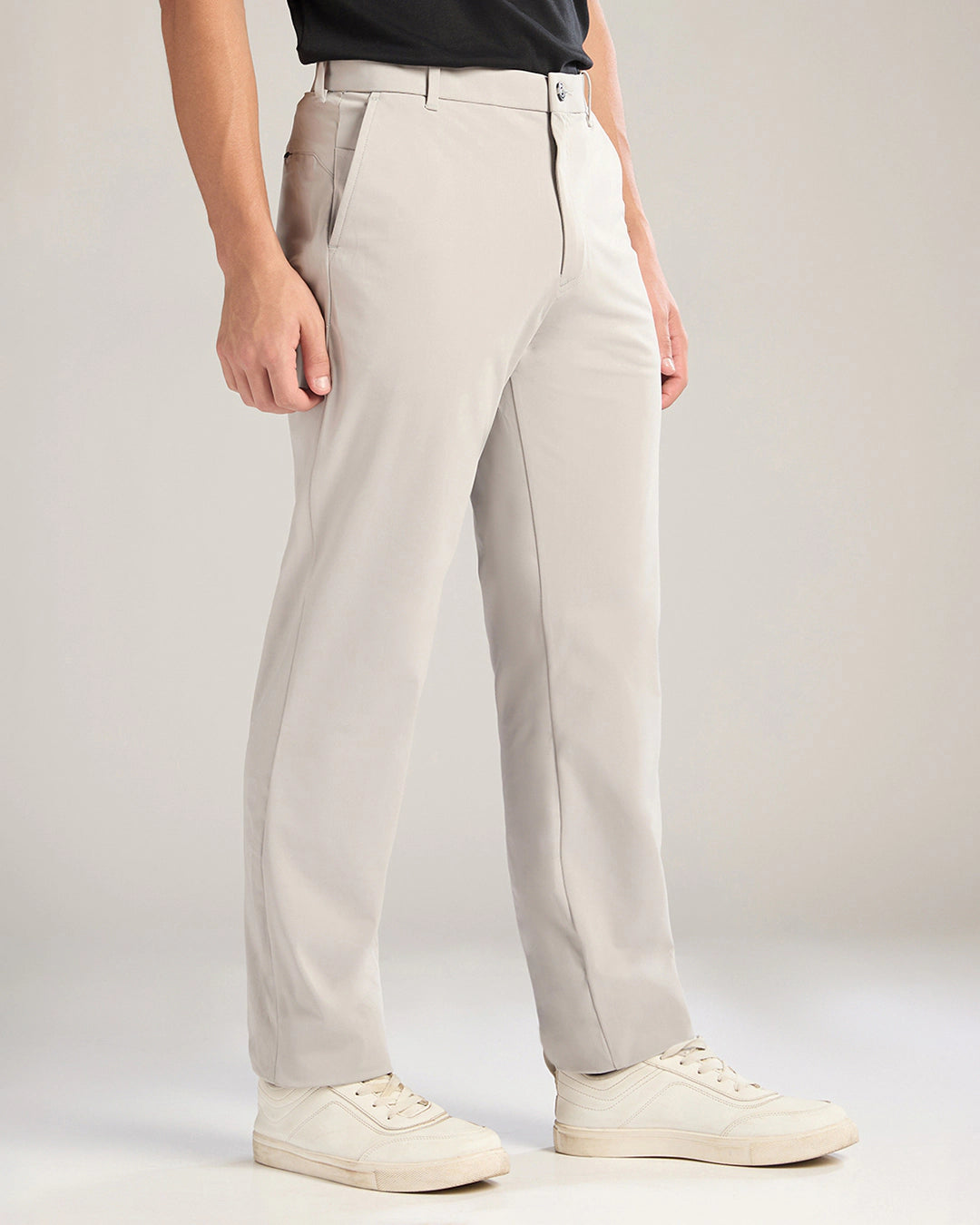 Person wearing light gray pants and white sneakers on a plain background