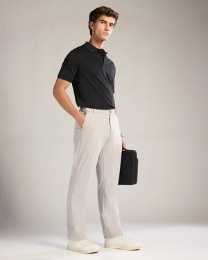 Man wearing a black polo shirt and light gray pants holding a black briefcase against a plain background