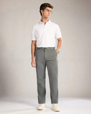 Man wearing a white polo shirt and gray pants against a plain background
