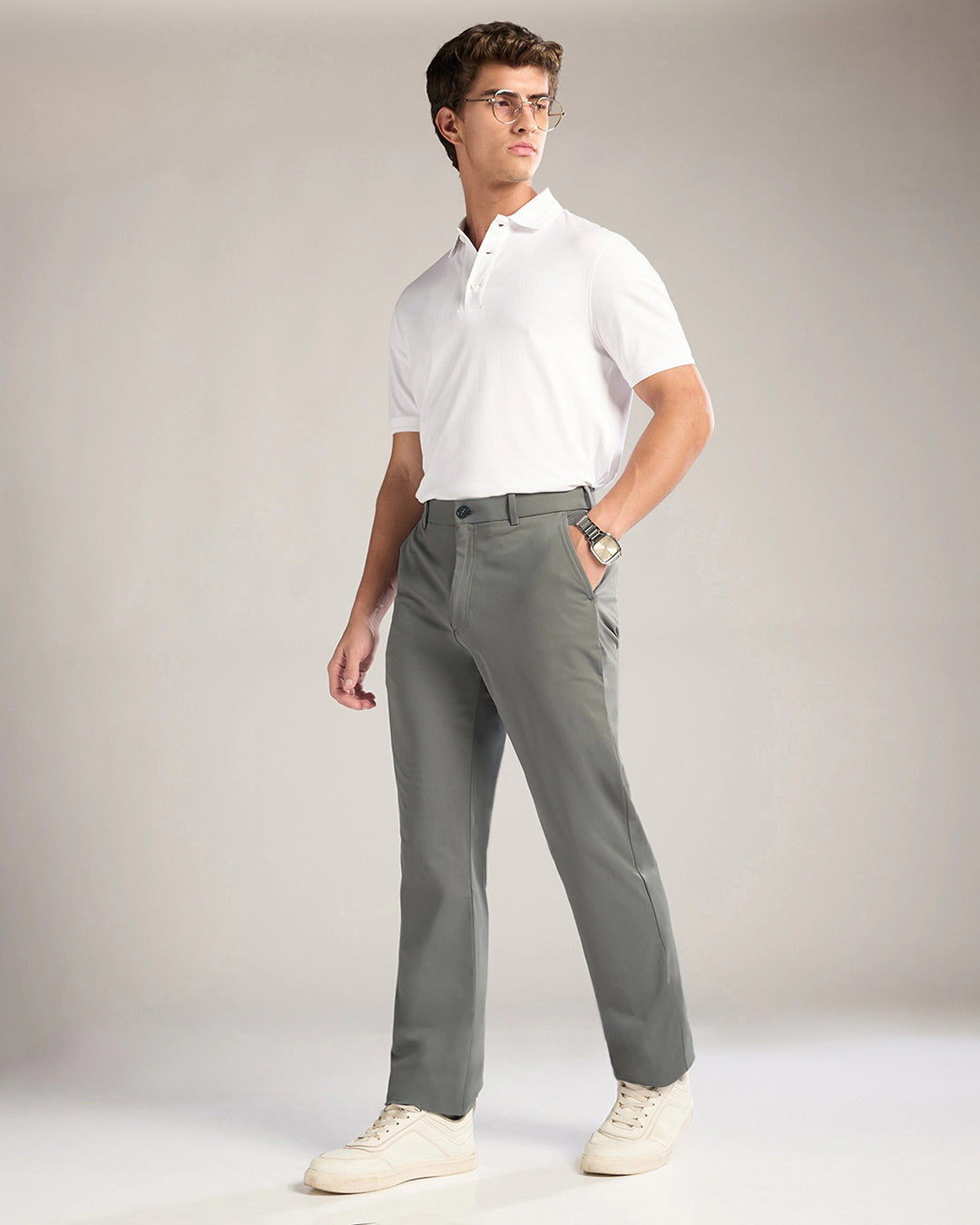 Man wearing a white polo shirt and gray pants against a plain background