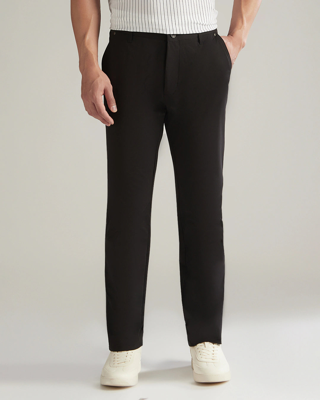 Person wearing black dress pants with a white shirt and white shoes on a light gray background