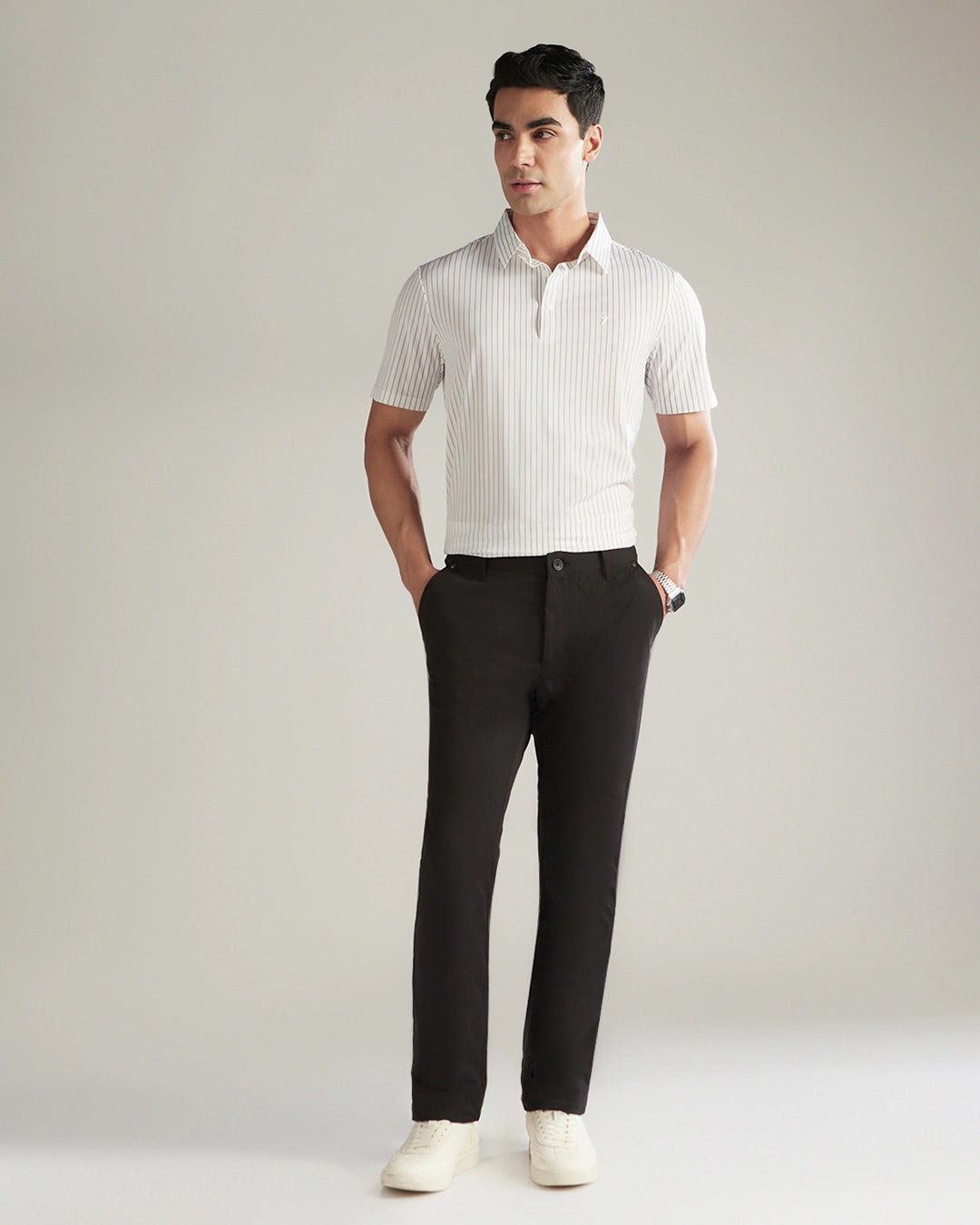 Man wearing a white striped polo shirt and black pants on a plain background