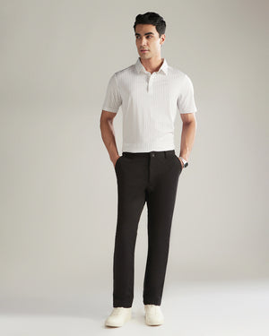 Man wearing a white striped polo shirt and black pants on a plain background