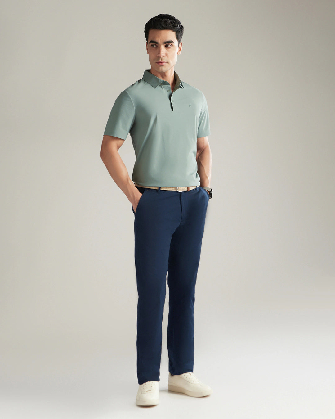 Man wearing a light green polo shirt and navy pants against a plain background